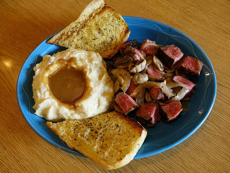 Diced steak with onions, with side of garlic bread and mashed potatoes